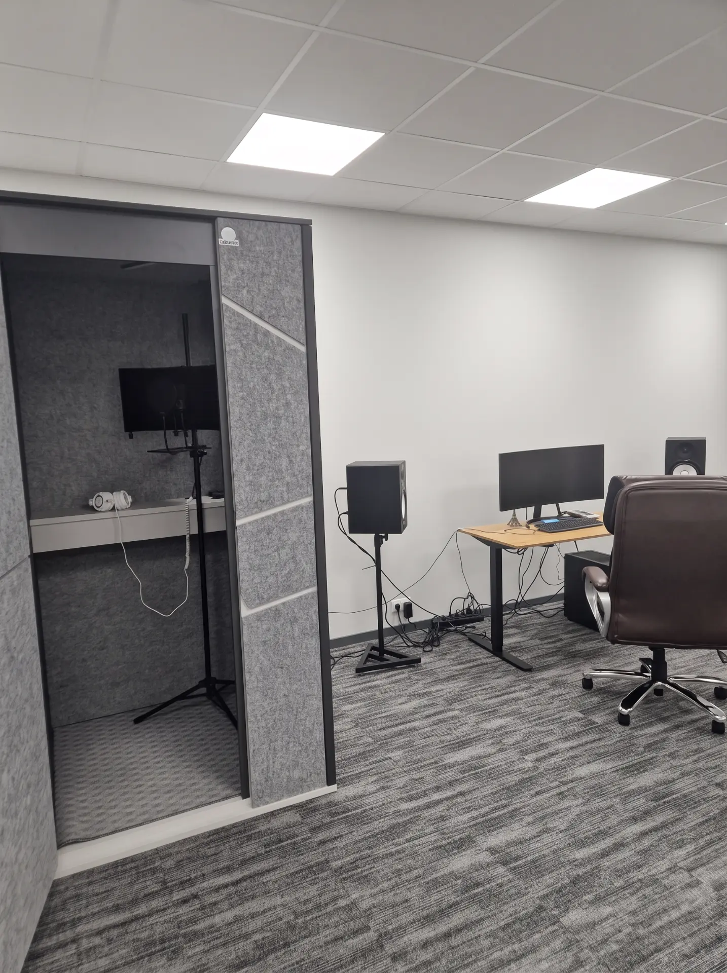 Studio overview with the vocal booth, recording desk and monitor speakers